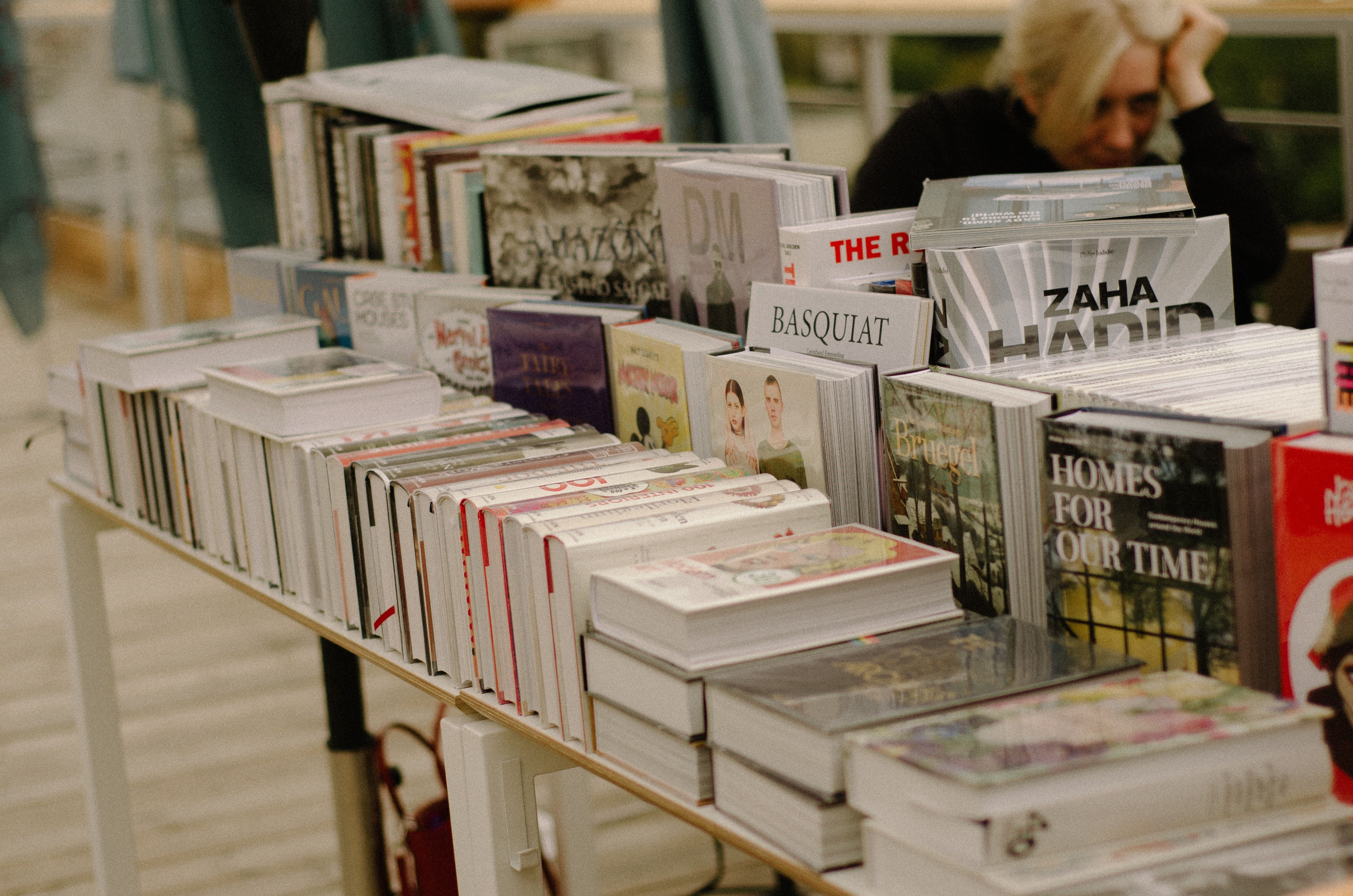 Books on a table for sale with woman browsing in the back